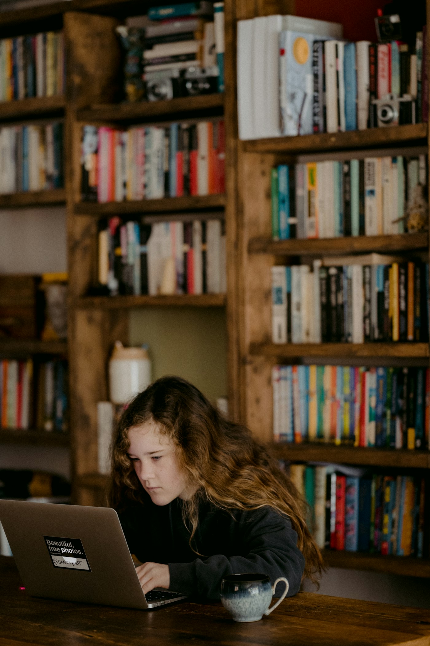 A teenage girl studying on a laptop in front of a bookcase